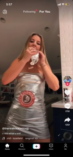 a woman in a silver dress is taking a selfie with her cell phone and eating food