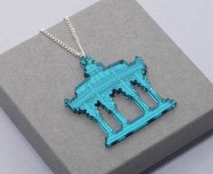 a blue necklace with a building in the middle on top of a gray box next to a silver chain