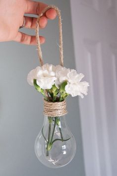 a person holding a glass vase with flowers in it and rope hanging from the ceiling