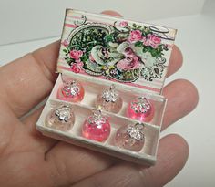 a hand holding a small box with six pairs of pink and white earrings in it