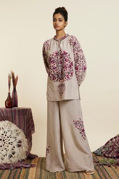 Grey crepe top with contrast flower vase, floral motifs, thread, sequin embroidery and layered loop tassel details. Paired with embroidered flared pants.
Components: 2
Pattern: Embroidered
Type Of Work: Thread, Sequin Work
Neckline: Frill Neck
Sleeve Type: Dolman Sleeves
Fabric: Crepe
Color: Grey
Other Details: 
Side slits
Embellished tassels
Embroidered sleeve cuffs
Top Closure: Front tasselled tie-up
Occasion: Work - Aza Fashions Coord Sets, Anita Dongre, Coord Set, Cuffed Top, Crepe Top, Sequin Embroidery, Top And Pants Set, Types Of Work, Indian Fashion Dresses