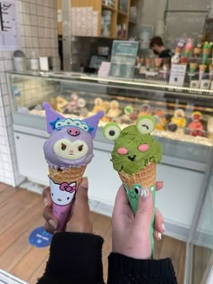 two people holding up ice cream cones with animals on them