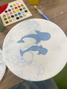 a plate with a dolphin on it sitting on a table next to paintbrushes