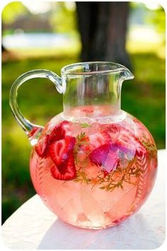 a pitcher filled with pink liquid sitting on top of a white table covered in flowers