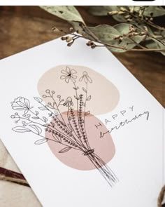 a card with some flowers on it sitting on top of a piece of paper next to a plant