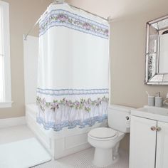 a white toilet sitting next to a bath tub under a bathroom mirror and shower curtain