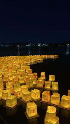 there are many lit cubes on the ground by the water at night with lights in them