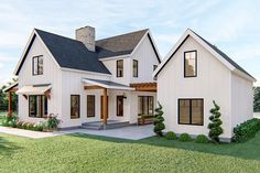 a white house with black roof and windows on the front porch is surrounded by greenery