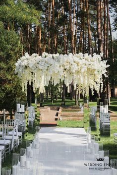 an outdoor ceremony setup with white flowers and candles on the aisle, surrounded by tall trees