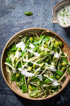 a bowl filled with green vegetables next to a cup of yogurt on a table