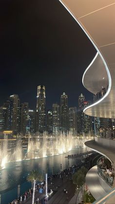 the city skyline is lit up at night with fountains in the water and people walking around