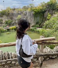 a woman standing on top of a wooden bridge next to a lake in the middle of a forest