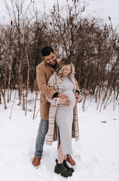 a pregnant couple cuddle in the snow