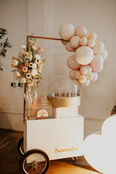 an ice cream cart with balloons hanging from it's sides and flowers in the back