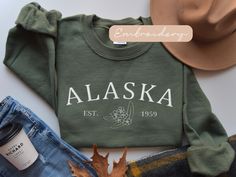 Embrace the spirit of the Last Frontier with our meticulously embroidered Alaska sweatshirt, a cozy tribute to the wild and beautiful North. Stay warm and show your love for Alaska in style with this must-have addition to your wardrobe. ✨DESCRIPTION✨  🌟GILDAN 18000 Unisex Sweatshirt - Embroidered design *100% cotton (Sport Grey is 90% cotton, 10% polyester; Ash Grey is 99% cotton, 1% polyester, heather colors are 50% cotton, 50% polyester. *Sweatshirts are in UNISEX sizing. Select your usual size for a more fitted look, or size up for a more relaxed fit. *Please note that the embroidery design has a backing on the inside of the sweatshirt to support the fabric and stitches. *Fabric Weight 5.0-5.3 oz/yd² (170-180 g/m²) *pre-shrunk jersey knit, air jet spun yarn for a soft feel & reduced pi Alaska Sweatshirt, Alaska Moose, Elizabeth Bennet, Family Cruise, Alaska Cruise, Womens Sweater, Sweater Gift, Cozy Sweatshirts, Pride And Prejudice