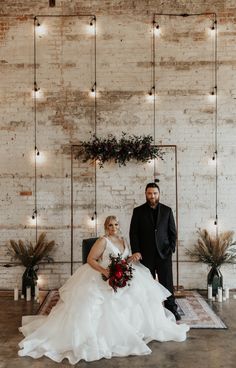 a bride and groom standing in front of a white brick wall with lights on it