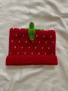 a crocheted strawberries purse is laying on a white sheet with a green leaf sticking out of it