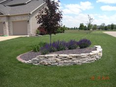 a stone wall in front of a house with purple flowers growing out of the middle