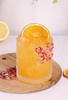 a glass filled with orange juice and garnished with pink flowers next to sliced lemons