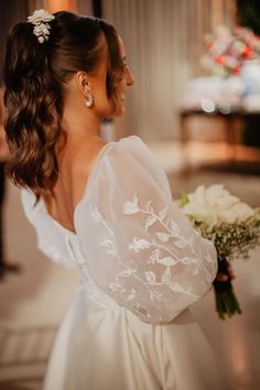 a woman in a white dress holding a bouquet and looking off into the distance with her back to the camera