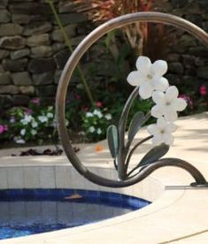 a metal sculpture with white flowers on it next to a pool