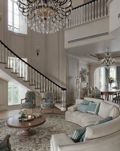 a living room filled with furniture and a chandelier hanging from the top of a stair case