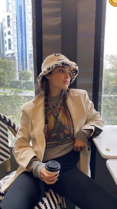 a woman sitting on top of a chair next to a window holding a coffee cup