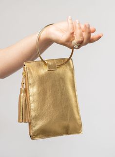 This bag is made from high-quality, super-soft metallic gold leather sourced from a premiere hide house in California. The leather is shipped to New York City, where our bags are produced by expert craftsmen and finished with a smooth zipper, leather tassel, and metal ring. Just big enough for all your essentials, we designed the Ring Wristlet to be your go-to bag for going out! Whether you’re heading to a cocktail party, a concert, or out on the town, slip it on your wrist so your hands are fre Modern Gold Clutch With Detachable Handle, Luxury Gold Bag With Smooth Grain, Chic Gold Leather Clutch, Gold Leather Bag With Smooth Grain, Gold Soft Leather Evening Clutch, Elegant Gold Clutch With Soft Leather, Evening Gold Soft Leather Clutch, Gold Leather Pouch Clutch, Modern Gold Clutch With Removable Pouch