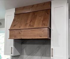 a kitchen with white cabinets and marble counter tops, an oven hood made out of wood