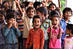 a group of children standing next to each other with their hands in the air and smiling