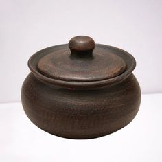 a brown pot with a wooden lid on a white surface