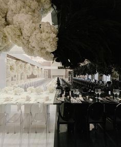 the tables and chairs are set up for a formal event with white flowers hanging from the ceiling