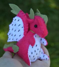 a hand holding a small red and white stuffed animal in it's left hand