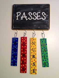 four colorful wooden name tags hanging on a white wall next to a chalkboard that says passes