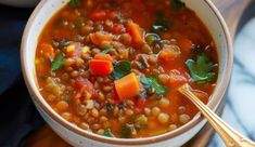 a bowl of soup with carrots, beans and spinach on a wooden board