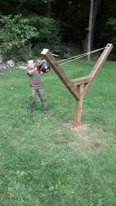 a young boy holding a skateboard and standing next to a wooden structure in the grass