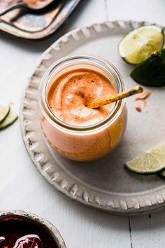 there is a small glass jar filled with liquid and limes on the plate next to it