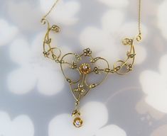 "Petite floral elements, swirling gold vines, tiny seed pearls and diamonds make up this beautiful antique 14k gold lavalier necklace. The artistic styling of this early 1900s piece is reminiscent of Victorian and Edwardian design. The necklace is composed with four main components, the gold chain, focal pendant and two fancy metalwork links flanking it. Most of the gold leaves and flower shapes are set with 0.5mm - 1mm seed pearls. Two are set with diamonds. The central pendant has a 2.1mm .01 Victorian Gold Jewelry With Flower Pendant, Edwardian Design, Lavalier Necklace, Art Nouveau Gold Filigree Necklaces, Art Nouveau Yellow Gold Gemstone Necklaces, 14k Gold Art Nouveau Pendant Necklace, Gold Art Nouveau Necklace With Gemstone, Flower Shapes, Gold Jewellery Design Necklaces