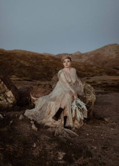 a woman sitting on top of a dirt field next to a pile of rocks and grass