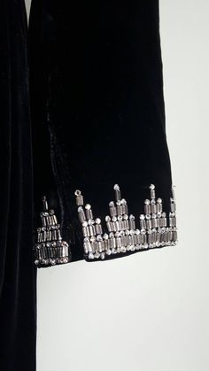 Dripping with deco diamentes 💎🗼 This exquisite gown in a rare larger size features allover inky black silk velvet; intricate, heavy, deco-look prong-set beads along the neckline and cuffs; a metal zipper in back and at both wrists; a dramatic empire waist and long sleeves and a long fit-and-slight-flare silhouette; and a full lining. This piece was sold with a satin crepe tie belt, which may or may not be original to the piece (there are no belt loops), but which is included in purchase. This Vintage Beaded Party Outerwear, Black Art Deco Embellished Dress, Luxury Vintage Beaded Outerwear, Vintage Black Velvet Outerwear, Luxury Embroidered Black Sequin Fabric, Long Formal Gowns, Tambour Embroidery, Exquisite Gowns, Formal Gown