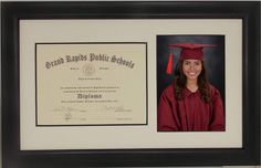 a woman wearing a graduation cap and gown in front of a black framed diploma certificate