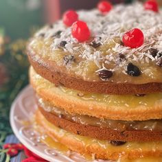 a stack of cake on top of a white plate covered in coconut and cherries