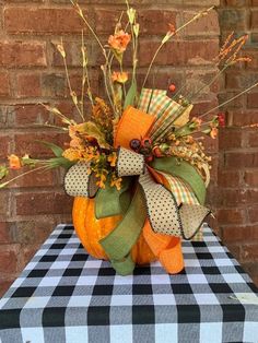 a pumpkin decorated with ribbon and flowers on top of a checkered tablecloth covered table