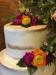 a three tiered white cake with flowers on top and greenery around the edges