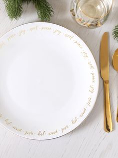 a white plate with gold lettering on it next to two golden spoons and forks