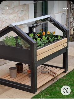 a small greenhouse with plants growing in it on a wooden platform next to a building