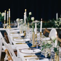 the table is set with white and blue linens, gold place settings and candles