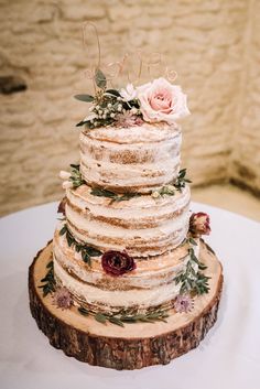 a wedding cake sitting on top of a wooden slice covered in frosting and flowers