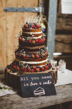 a wedding cake with strawberries and berries on top is displayed next to a sign that says, all you need is love & cake