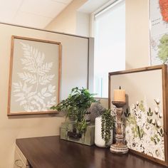 two framed pictures and some plants on a table